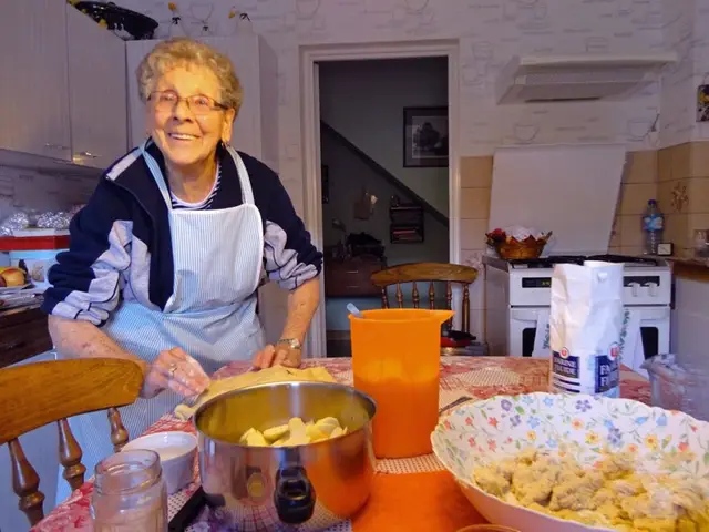 Jeanne, souriante dans sa cuisine, en tablier, en train de cuisiner.